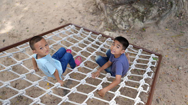 A two children play on climbing net, smiling and enjoying their time outdoors. scene captures joy of childhood and fun of physical activity in natural setting