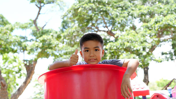 A cheerful child enjoying playtime in bright red play structure, giving thumbs up gesture. background features lush green trees, creating vibrant outdoor atmosphere