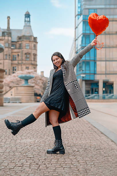 istock Woman joyfully poses with a heart-shaped balloon in a city square during springtime while wearing a stylish coat and boots 2220159640