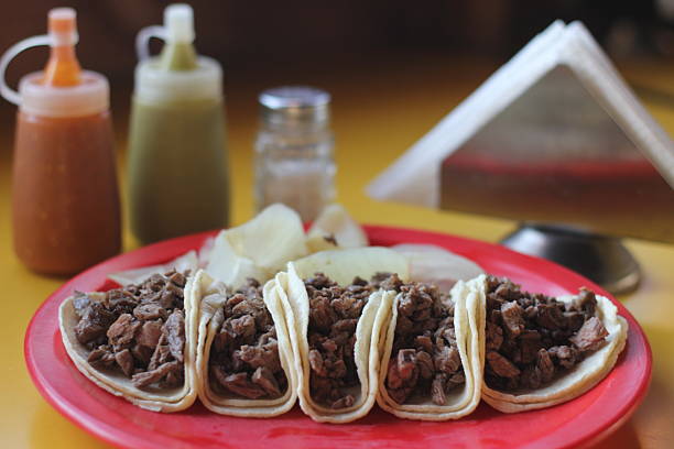 Street tacos, filled with savory birria or carne asada, topped with diced onion and cilantro, and served on warm corn tortillas with a side of salsa
