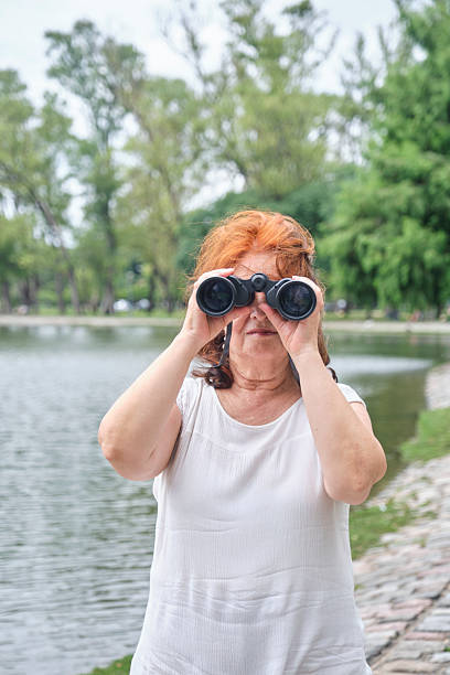 Senior Hispanic woman using binoculars, portrait looking at camera. Concept: The wellbeing of maintaining an active lifestyle in contact with nature.