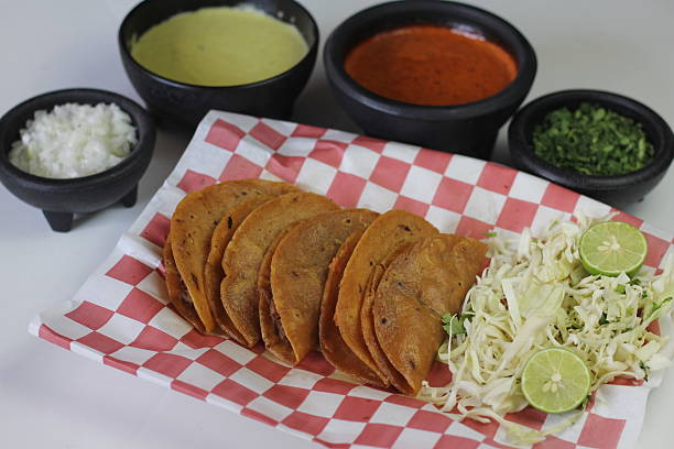 An enticing collection of savory crispy tacos accompanied by fresh sides including lime, cabbage, and a trio of flavorful salsas, perfect for satisfying any appetite.