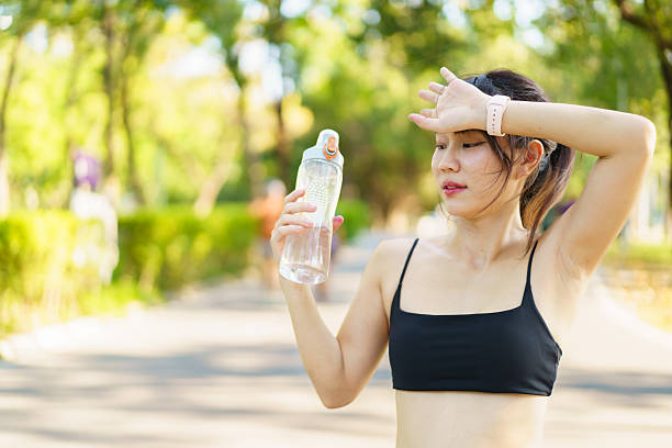 istock Asian woman take a break and drinks water from bottle after finished running. 2220173537
