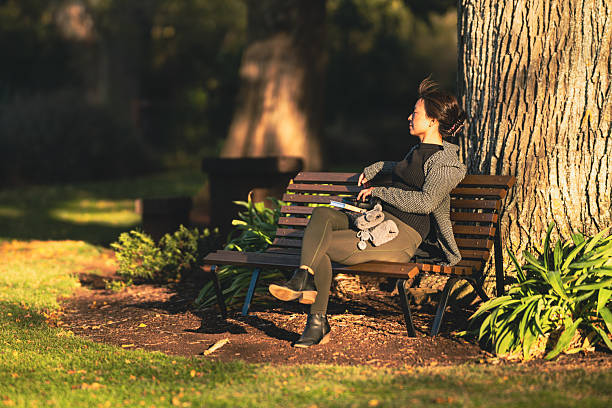 Sunlight shining on a woman sitting on a bench in the park, Camperdown Botanic Gardens, Camperdown, Victoria, Australia