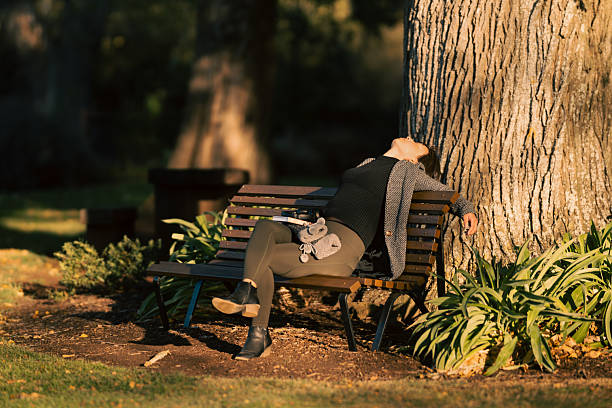 Sunlight shining on a woman sitting on a bench in the park, Camperdown Botanic Gardens, Camperdown, Victoria, Australia