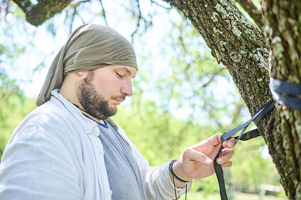 Young hispanic man hanging a hammock from the trees, to rest in nature. Concept: enjoying leisure time outdoors.