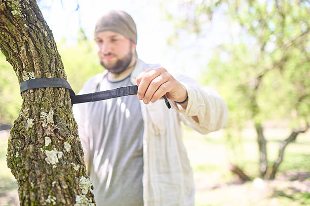 istock Young man tying a black sling to a tree to hang a hammock. 2220193672
