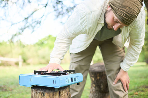 Young hispanic man about to cook outdoors on a light blue portable stove while camping at a nature campground.