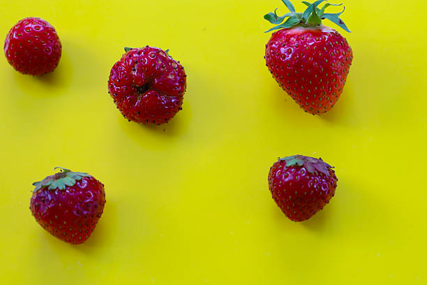 Bright red strawberries are scattered haphazardly on a vibrant yellow background, creating a dynamic and appealing composition. This striking contrast is ideal for summer and culinary themes.