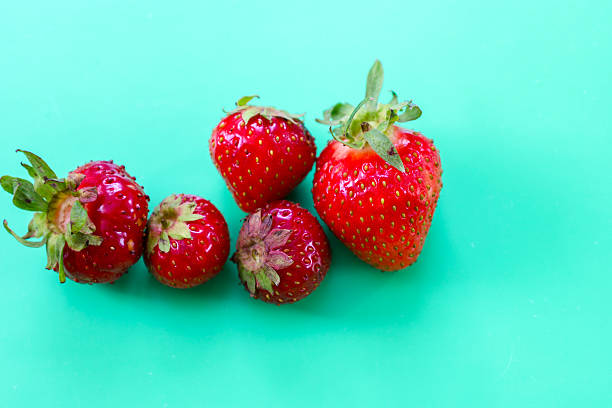 Juicy red strawberries are lined up on a vibrant turquoise background, creating a fresh and inviting composition. This striking color contrast is ideal for summer and culinary themes.