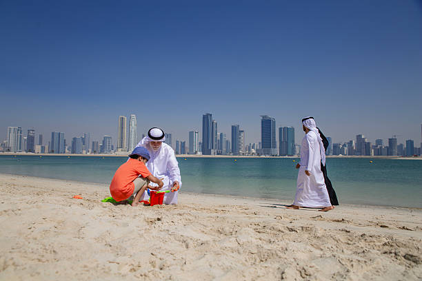 Middle eastern grandpa and grandson playing game with colorful sandcastle toys on the sandy beach.