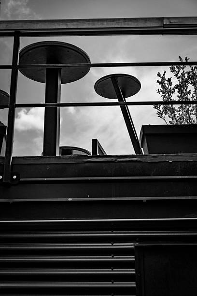 A compelling black and white photograph of a cafe built over a metal container structure. The image portrays a creative repurposing of industrial materials to create a unique and inviting space. It’s a commentary on adapting the rigid, structured world for everyday enjoyment.