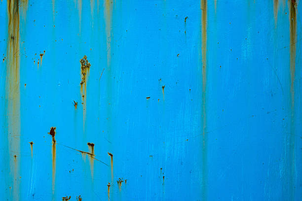 Rusty metal surface showcases intricate patterns formed by rusting and weathering. Outdoor industrial setting captures a sense of age and decay under bright daylight.