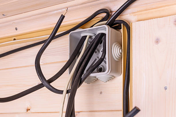 istock Open electrical junction box with multiple black and white wires protruding in wooden wall, showing installation stage and safety importance. 2220215039