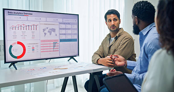 istock Group of business professionals meeting reviewing global data analytics presented on a large screen, discussing strategy and growth at the office. Finance meeting concept. 2220215530
