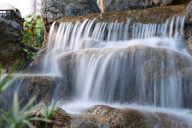 A pondless backyard waterfall. Three bronze turtle statues sit on the rocks and is surrounded with red mulch, juniper bushes, holly bushes, and a Japanese maple tree.