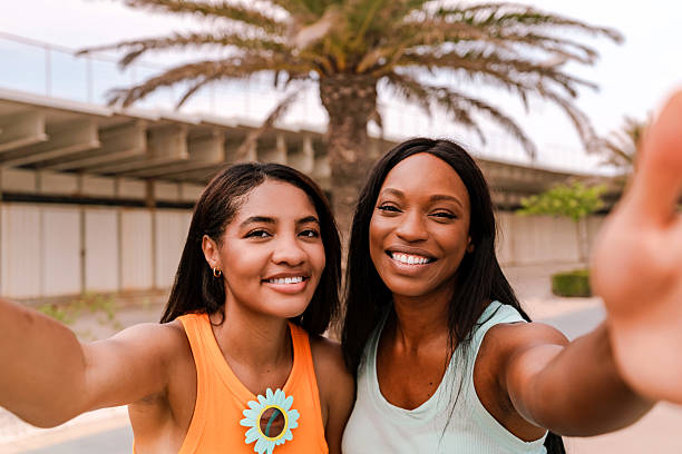 istock Two multiracial friends taking a selfie on a sunny day under a palm tree 2220217384