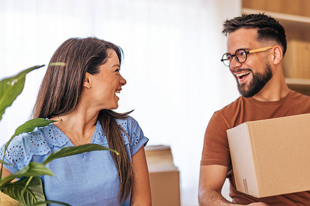 istock Happy couple carrying boxes and plant into new home while laughing 2220218507