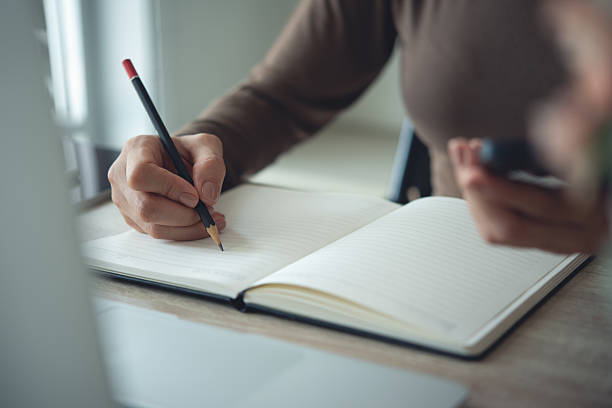 istock Close up, Woman hand with a pencil writing on paper notebook with laptop computer on office table. Business woman taking note on notebook, planning work schedule. Student study online, e-learning 2220219225