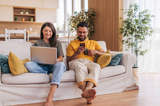 istock Young couple relaxing on sofa using laptop and smartphone 2220220283