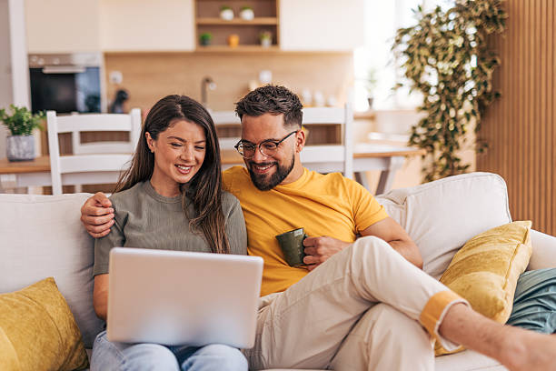 istock Young couple relaxing on sofa browsing internet on laptop 2220220288