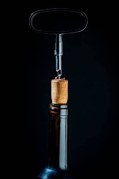 istock Opening a glass wine bottle with corkscrew on black background, closeup 2220220496