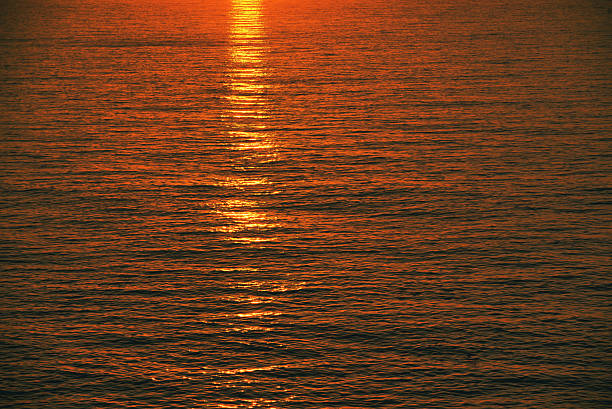 The water is calm and the sun is setting, creating a beautiful reflection of the sun on the water
