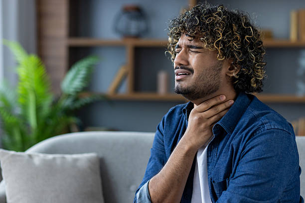 istock A man experiencing throat pain, possibly from illness, while sitting on a comfortable sofa. 2220225939