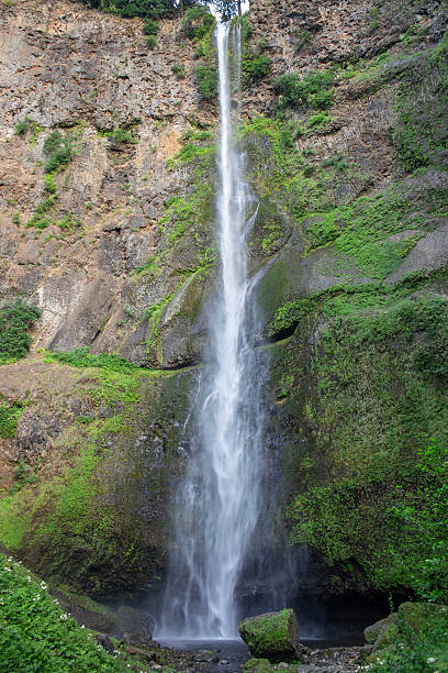 istock Majestic waterfall cascades down rocky cliffs surrounded by lush greenery on a bright sunny day 2220226450