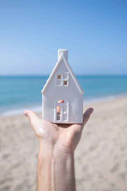 istock Hand holding small white house model on beach 2220231422