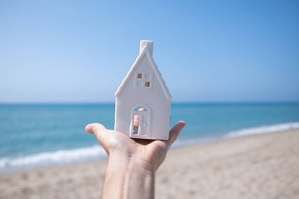 istock Hand holding small white house model on beach by the sea 2220231749