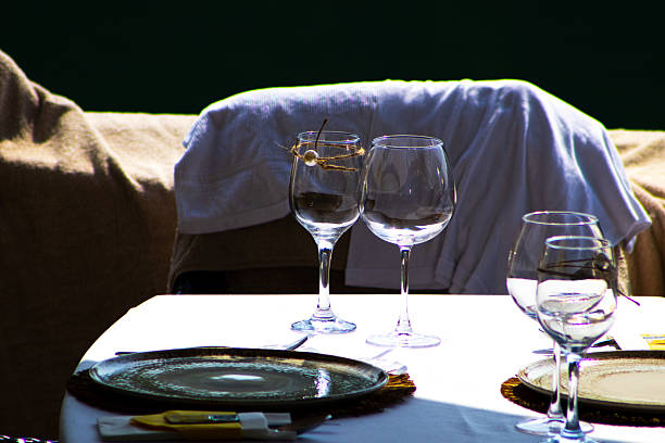 An outdoor dining table on what appears to be a boat deck is set with four place settings, including dark plates and wine glasses