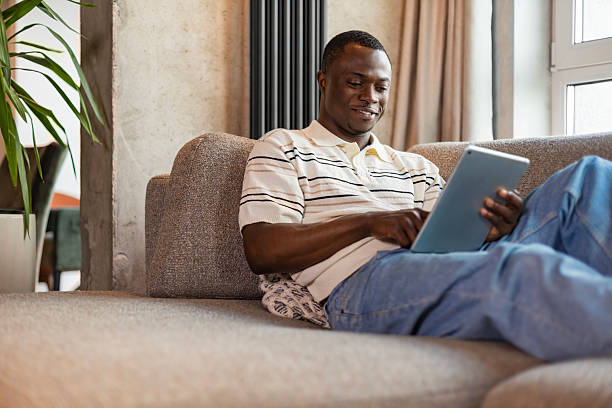 istock Smiling handsome african man holding and using tablet with social networks at home, happy freelancer making online shopping, sitting on cozy sofa at living room 2220232872