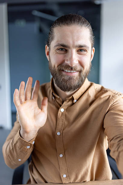 istock A smiling man waves to the camera, looking friendly and welcoming with a natural expression. 2220233182