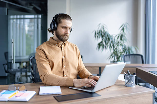 istock Professional man working on laptop with headphones in modern office workspace 2220233732