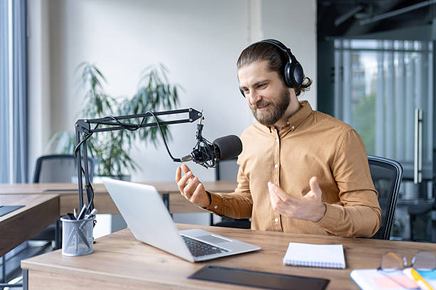 istock Bearded man recording a podcast episode in a modern office setting, using a professional microphone. 2220233741