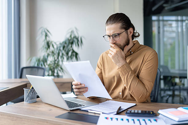 istock Thoughtful businessman reviewing documents in his office, pondering over details with a focused expression. 2220233746
