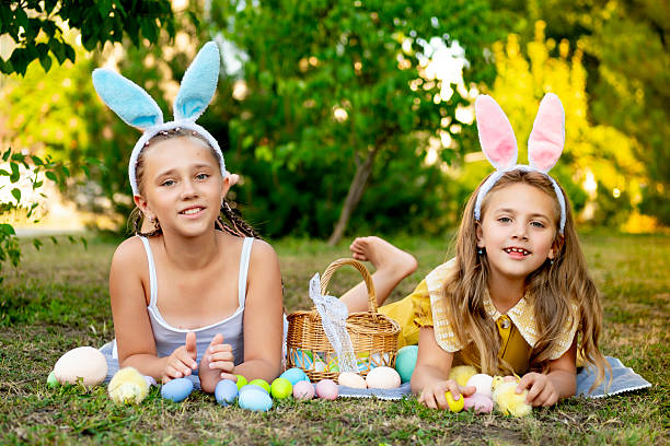 istock Easter, children play with Easter eggs in bunny ears on the green lawn. Easter tradition. Children with a basket full of colorful eggs 2220237879
