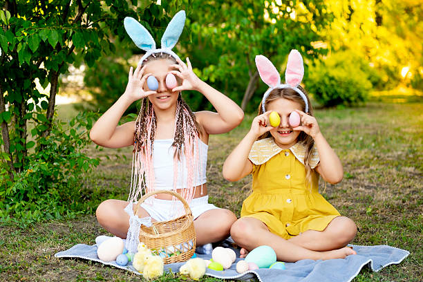 istock Easter, children play with Easter eggs in bunny ears on the green lawn. Easter tradition. Children with a basket full of colorful eggs 2220237917