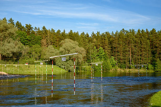 A river slalom course with numbered poles for kayaking or canoeing, surrounded by green forest under a blue summer sky.