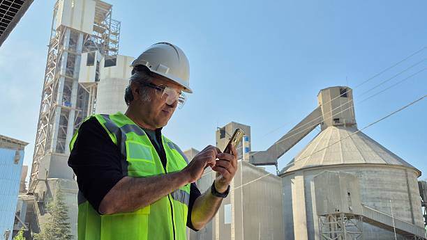 A serious industry worker is receiving important message on the phone while standing on high metal construction