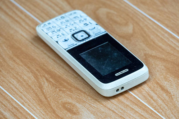 Old white feature phone with Bengali language and torch light on wooden surface. Used button mobile phone.