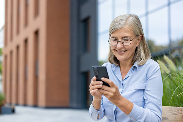 istock Smiling mature woman using her smartphone outside a modern building during the daytime. 2220248985