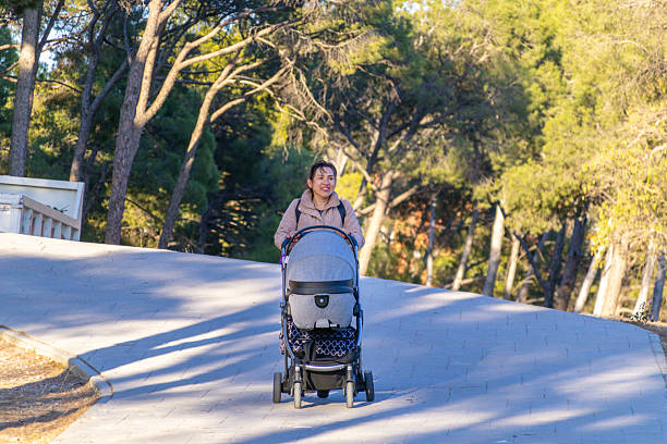 A happy mother takes a leisurely walk in a vibrant park on a sunny day. She pushes a stylish stroller, showcasing the bond between parent and child amidst nature's beauty.