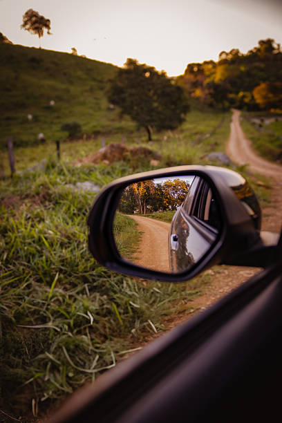 Dirt road and green fields being reflected in the car's rear view mirror