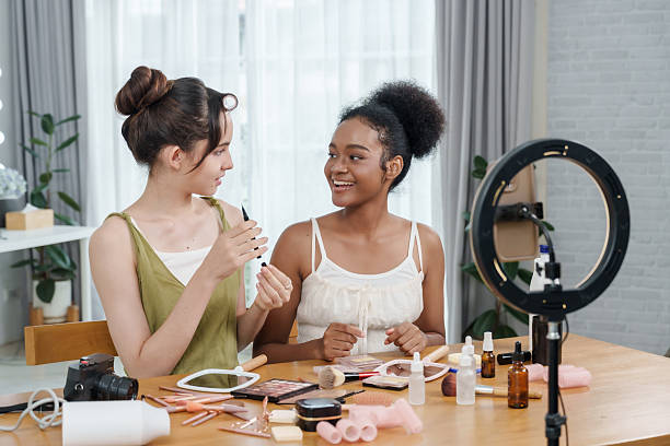 istock two multiracial female adults smiling while holding makeup tools filming cosmetic review video together sitting at table filled with skincare items camera ringlight and beauty products in bright room 2220264508