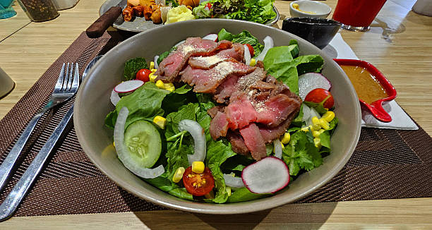 istock Sliced beef or meat salad on fresh vegetables, cucumber, lettuce, tomato, corn, onion and cabbage in white bowl. 2220266231