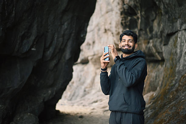 istock A young man smiles at the camera while capturing a shot with his phone inside a rocky mountain passage. 2220266609