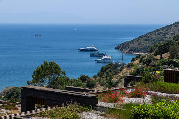 Muğla, Turkey – June 15, 2025:A picturesque panorama of a luxury resort's private bay, featuring its beach, pier, and various yachts, located on the coast of Bodrum, Turkey, in the vicinity of Bitez. The clear blue waters of the Aegean Sea reflect the bright summer sky, highlighting the area's appeal as a high-end tourist destination.