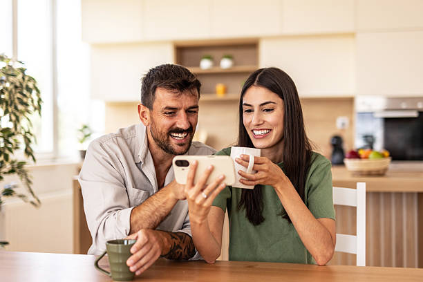 istock Happy couple watching smartphone and drinking coffee in kitchen 2220267683
